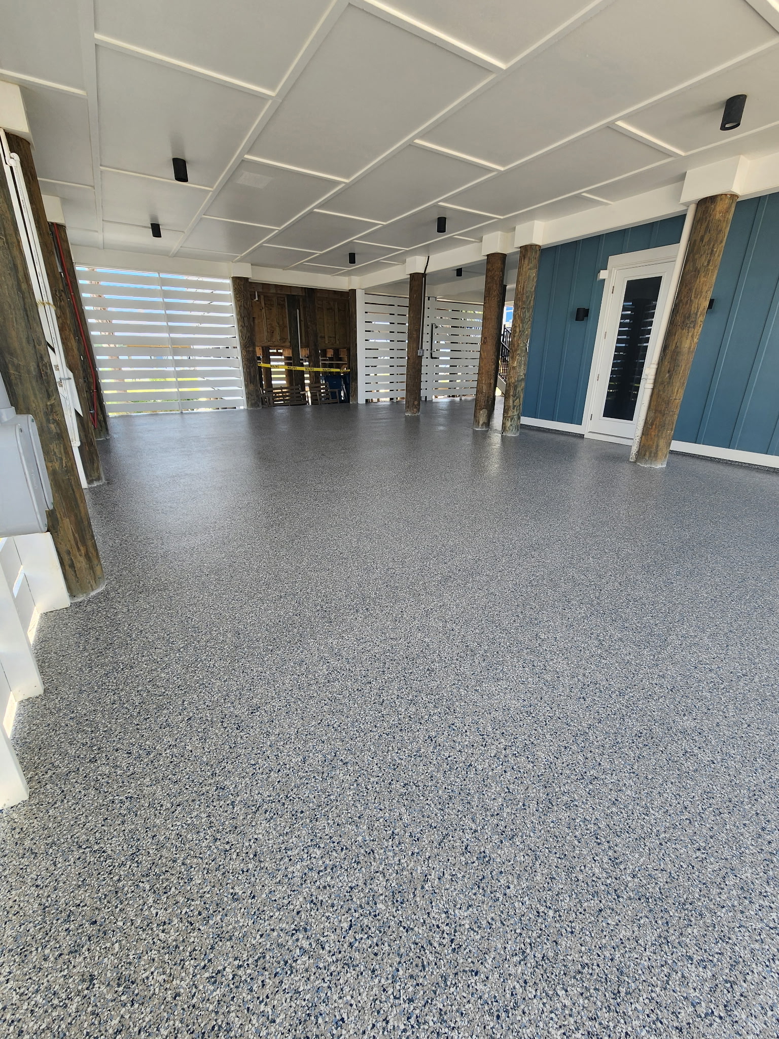 Spacious empty room with a speckled epoxy floor, brick columns, a blue accent wall with a doorway, and a brick fireplace at the far end.