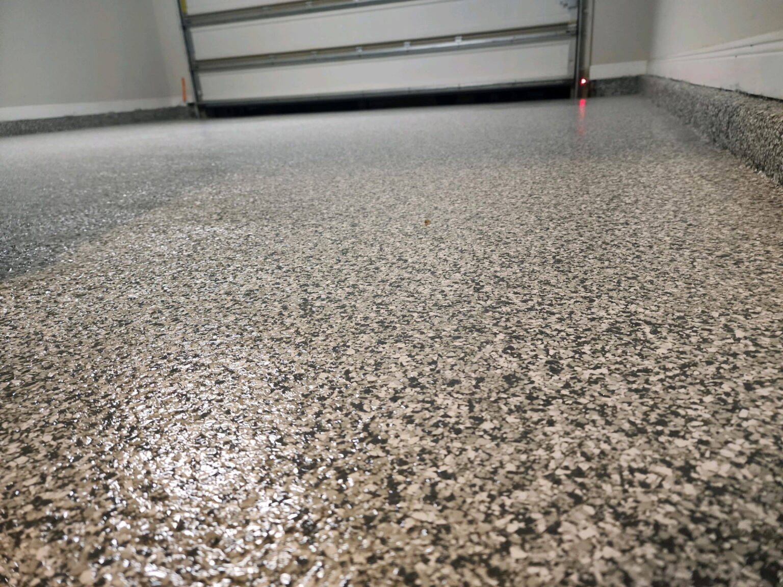 Low-angle close-up of a speckled epoxy garage floor with a closed garage door in the background.