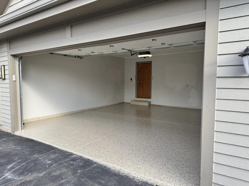 An empty residential garage with a light-colored floor, white walls, and a wooden door at the far end.