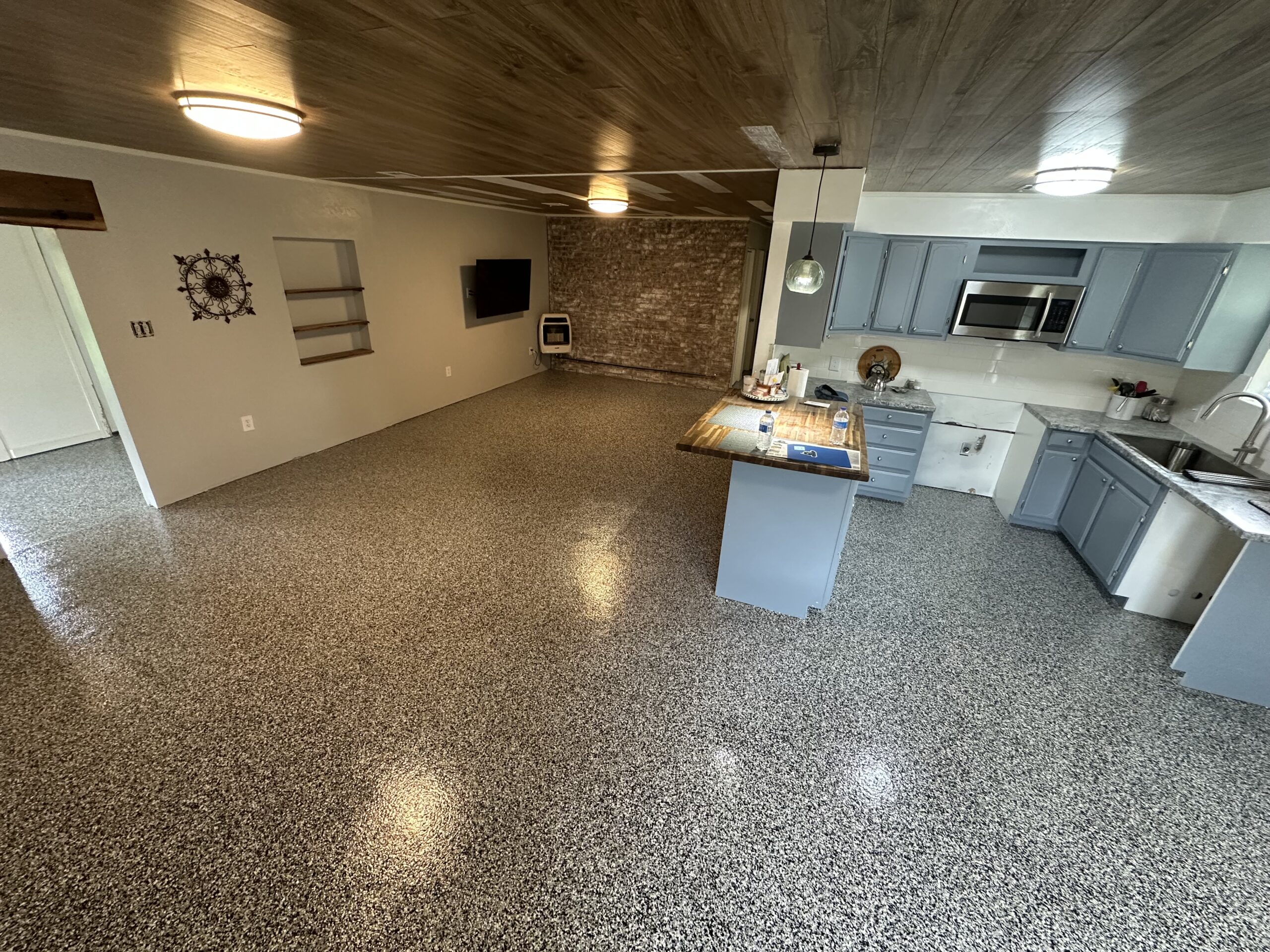 Open-concept kitchen with blue-gray cabinets and island, adjacent living area featuring a brick fireplace and wall-mounted TV.
